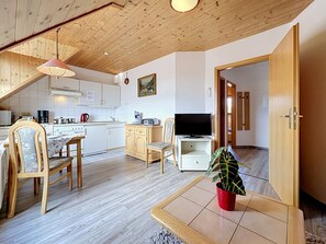 Una cocina moderna con armarios blancos, una mesa de comedor, sillas, un televisor y una planta en maceta.
