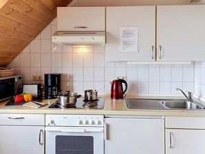 Uma cozinha com armários brancos, fogão, pia e diversos eletrodomésticos.