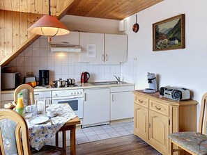 A compact kitchen with white cabinets, a stove, a sink, and a dining area with a table set for two.