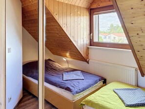 Un dormitorio con techo inclinado, una cama con cabecera, una lámpara de noche y una ventana con vistas a edificios.