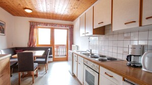A modern kitchen with wooden cabinets, a dining area with a table and chairs, and a view through a glass door to a balcony. - Voithofer by Interhome (Königsleiten)
