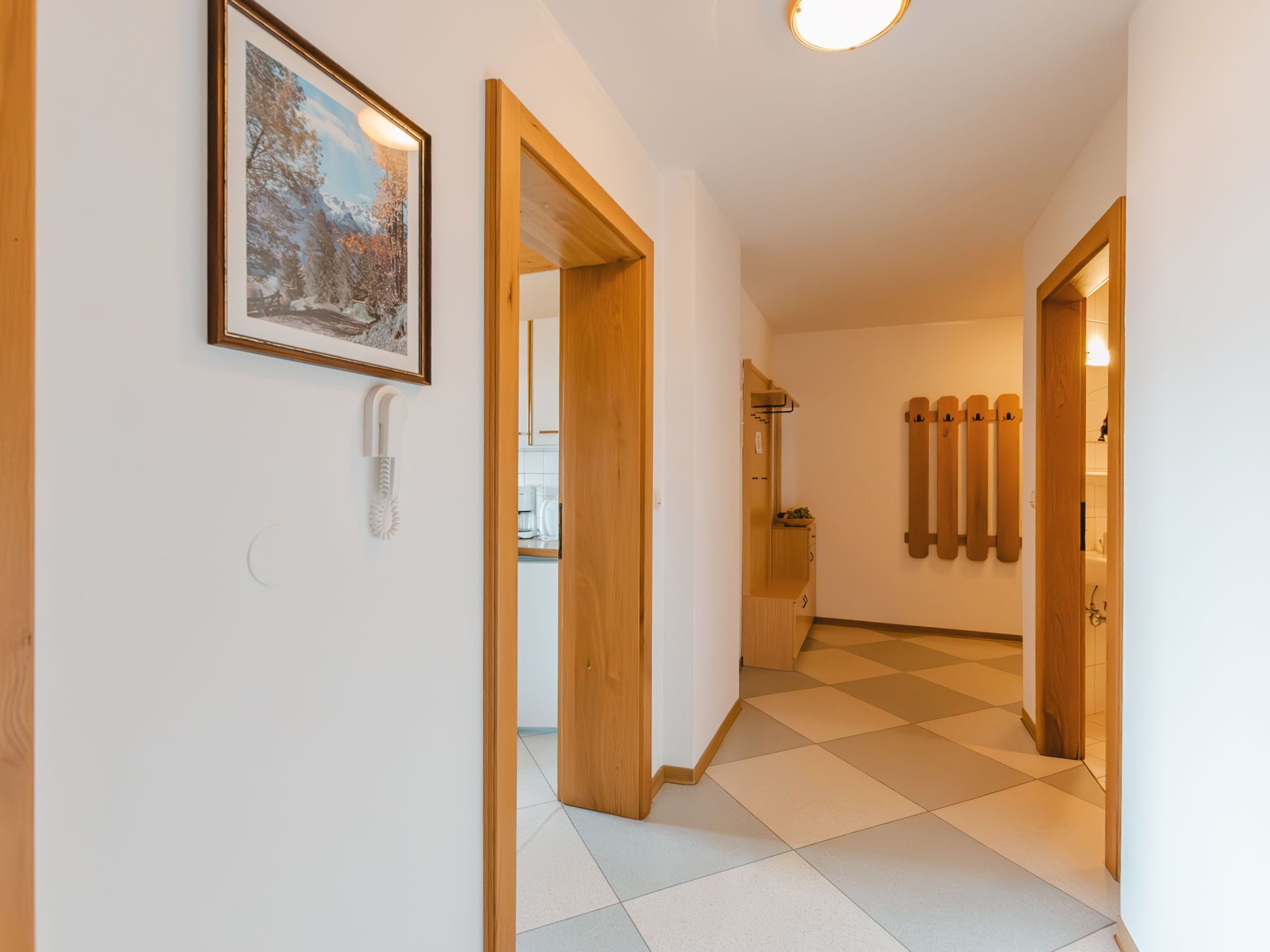A hallway with a checkered floor, wooden doors, a framed picture on the wall, and a light fixture on the ceiling.