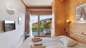 A bedroom with a large bed, a TV, and a view of a garden and mountains.