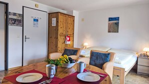 A hotel room with a dining table set for two, a bed with a nightstand, a wooden wardrobe, and a painting on the wall. - Rose Studio Y by Interhome (Wengen)