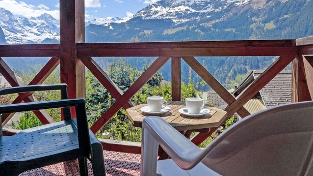 A wooden deck with a table and chairs overlooking a mountainous landscape. - Rose Studio Y by Interhome (Wengen)