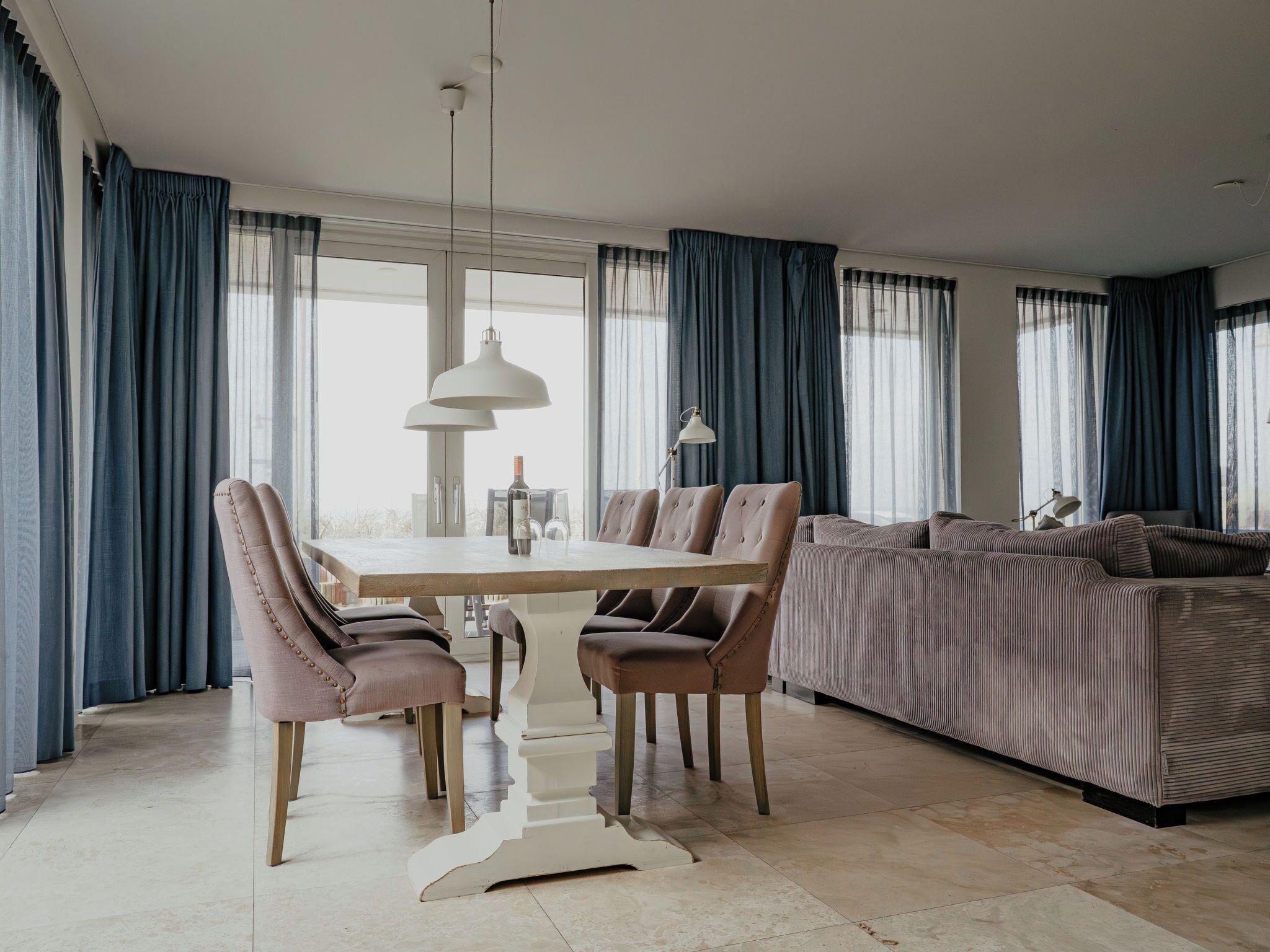 Un espace repas moderne avec une table et des chaises en bois, un luminaire suspendu et un canapé en arrière-plan.