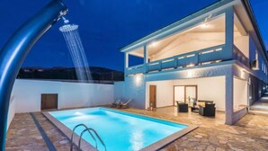 A modern outdoor pool area with a stone-tiled deck, a built-in jacuzzi, and a covered seating area with outdoor furniture. - Velebit by Interhome (Rovanjska)