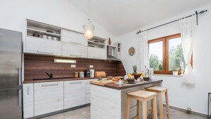 A modern kitchen with white cabinets, a wooden countertop, and a central island with stools. - Velebit by Interhome (Rovanjska)