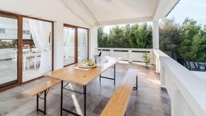 A modern outdoor dining area with a wooden table and benches, large sliding glass doors, and a view of trees. - Velebit by Interhome (Rovanjska)