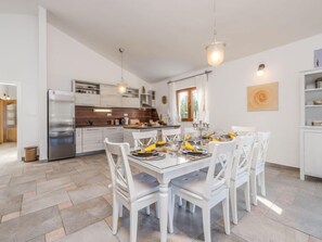 A modern kitchen with white cabinets, a stainless steel refrigerator, and a dining area with a white table set for four.