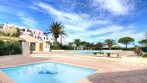 Ein Swimmingpool mit Delphin-Motiv, umgeben von Palmen und wolkenlosem, blauem Himmel.