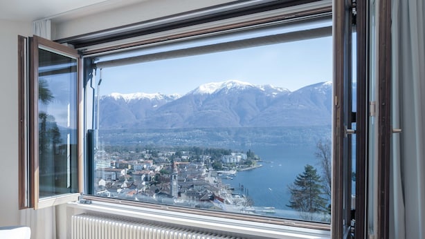 A room with a large window overlooking a lake and mountains. - Suite Classic by Interhome (Ascona)