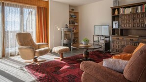 Un salon chaleureux avec un plafond haut, des poutres apparentes, une cheminée, un téléviseur et une bibliothèque.