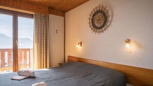 Une chambre avec un lit, deux lampes fixées au mur, un élément de décoration circulaire sur le mur et une vue par une fenêtre avec des rideaux.