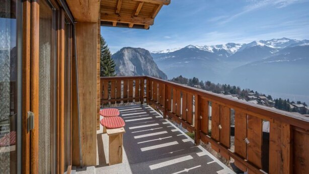 Un balcon en bois offrant une vue sur des montagnes enneigées.