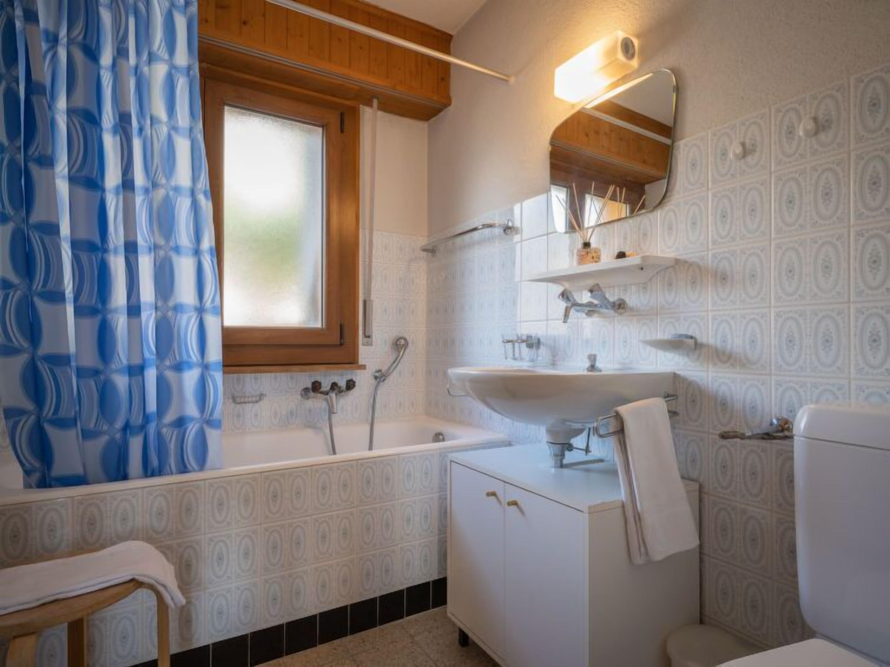 A bathroom with a bathtub, a sink, and a toilet. There is a window above the bathtub and a mirror above the sink.