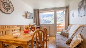Ein gemütliches Zimmer mit Holztisch, Stühlen, einer Couch und einem großen Fenster mit Bergblick.
