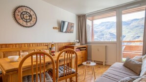 Ein gemütliches Zimmer mit einem Holzespeisetisch, Stühlen, einer Couch und einem großen Fenster mit Blick auf die Berge.
