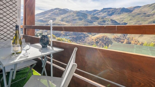 Ein Balkon mit Tisch, einer Weinflasche und Gläsern, mit Blick auf eine gebirgige Landschaft.