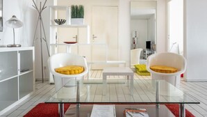 Un salon moderne avec des meubles blancs, une table basse en verre et un tapis rouge.
