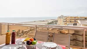Un balcon avec une table dressée pour le dîner, donnant sur une plage et des bâtiments.