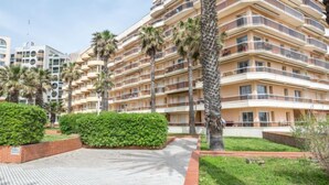Un hôtel à plusieurs étages doté de balcons, de palmiers et d’une promenade dallée.