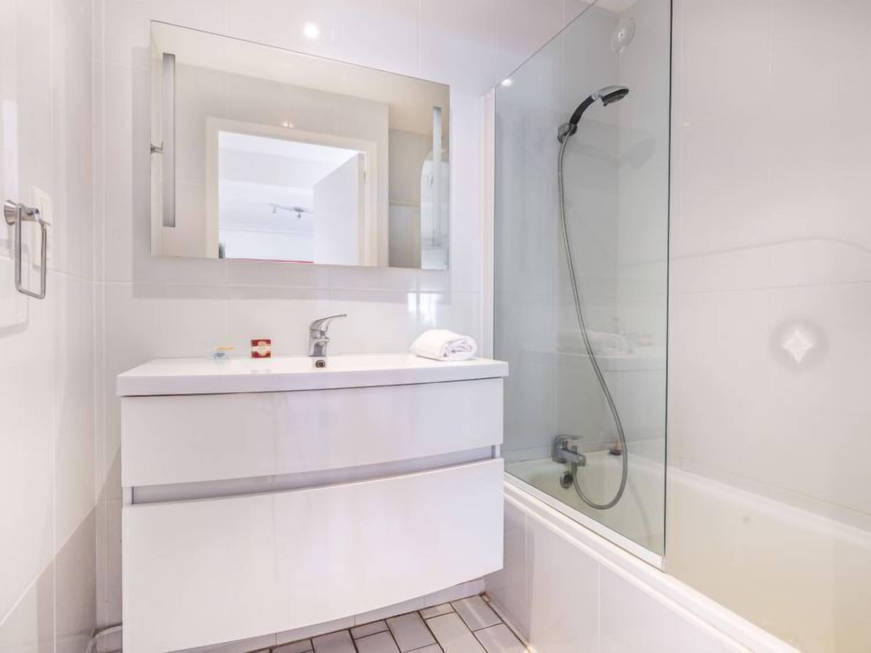 Une salle de bain moderne avec une douche à parois de verre, un meuble-lavabo blanc avec un miroir et des toilettes blanches.