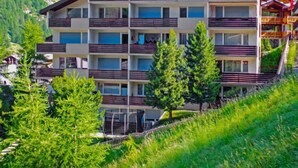 Un hôtel à plusieurs étages doté de balcons, entouré de verdure et de montagnes.