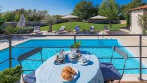 A poolside dining area with a table set for two, a chair, and a croissant. - Histria 1 by Interhome (Pula/Vodnjan)