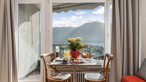 A dining area with a table set for breakfast, a view of mountains and a lake, and a red bench in the foreground. - Double Room Modern by Interhome (Ascona)