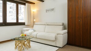 A living room with a glass table, a white sofa, a wooden wardrobe, and a window with curtains. - Residenza Chesa Margun 35-1 by Interhome (Silvaplana-Surlej)