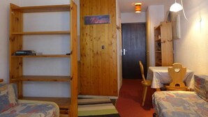 Une pièce de taille modeste, avec une bibliothèque en bois, un lit recouvert d’une literie à motifs, une petite table et une chaise.
