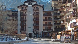 Un hôtel à plusieurs étages doté de balcons, d’une enseigne indiquant un service de location de matériel de ski, et avec une vue sur les montagnes en arrière-plan.