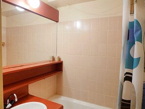Un baño con un lavamanos blanco, un espejo, una repisa roja y una cortina de ducha.