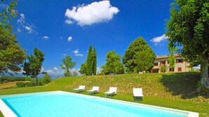 A rectangular swimming pool with a clear blue water surface, surrounded by a grassy area with four white lounge chairs aligned parallel to the pool. - Montebello by Interhome (Città di Castello)