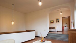 A spacious living room with a white sofa, a small white table with a floral centerpiece, and a staircase leading to a bedroom. - Montebello by Interhome (Città di Castello)