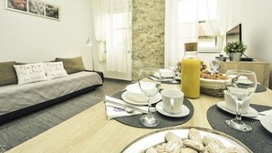 A modern, well-lit room with a sofa, dining table set with plates, glasses, and a fruit basket. - Snježana by Interhome (Karlobag)