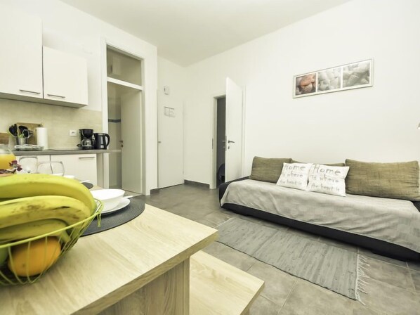 A modern, minimalistic room with a wooden dining table, a sofa with cushions, and a kitchen area with cabinets and a coffee machine. - Snježana by Interhome (Karlobag)