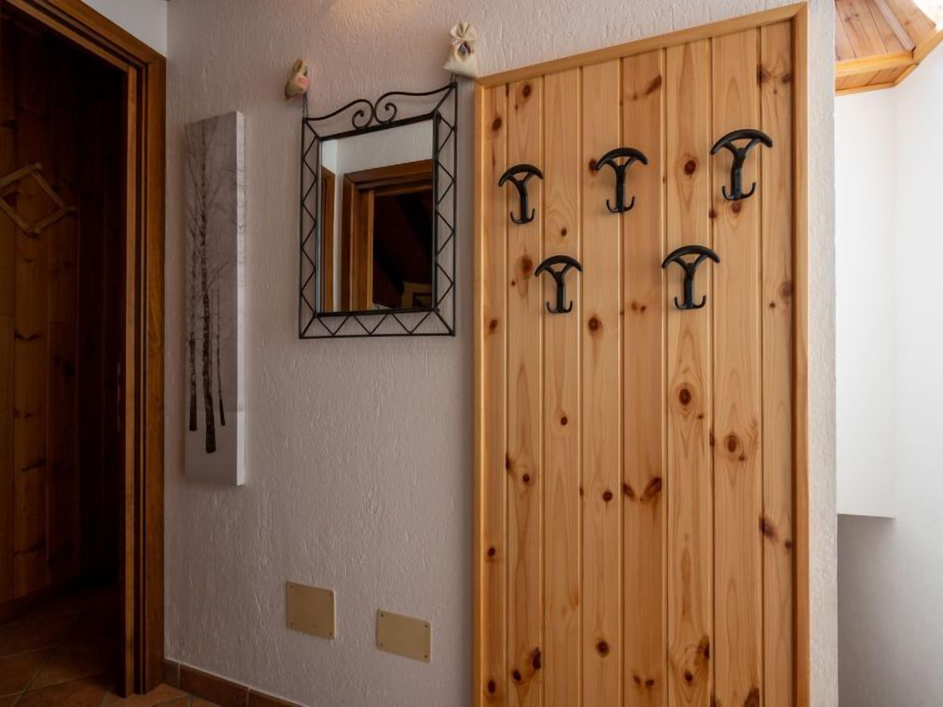 Eine Holztür mit fünf schwarzen Türhaken, ein Spiegel mit geometrischem Rahmen und zwei Lichtschaltern an der Wand.