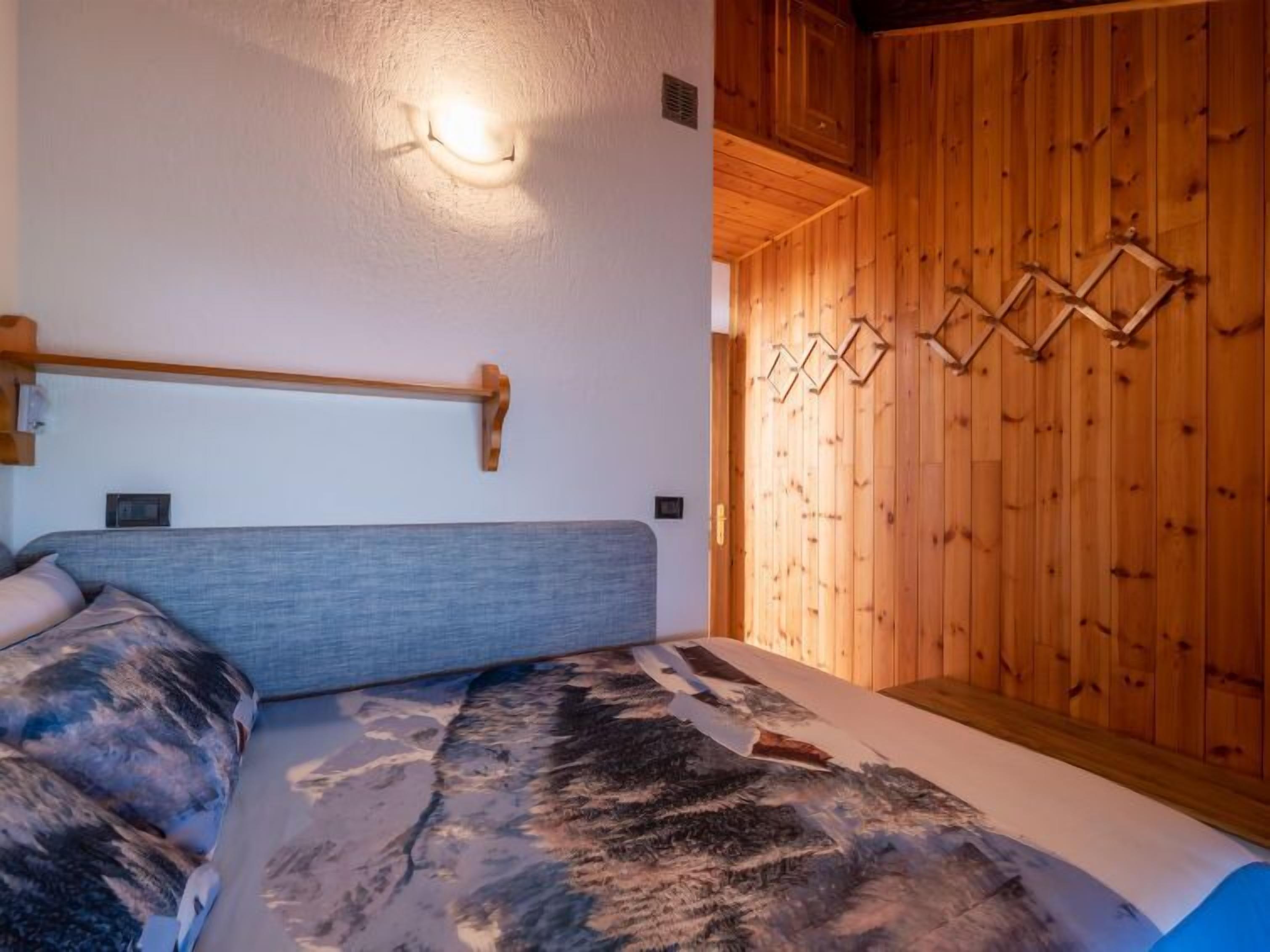 A bedroom with a bed, wooden wall paneling, and a light fixture.