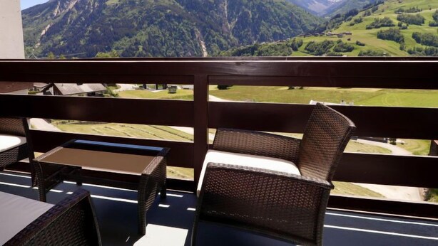 Un balcón con mobiliario de mimbre con vistas a un paisaje montañoso.