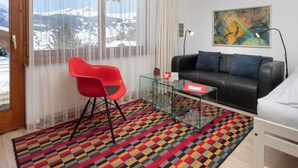 A modern room with a glass coffee table, a red chair, a black sofa, and a colorful rug.