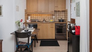 A compact kitchen with wooden cabinets, a dining table with chairs, a stove, and a refrigerator.