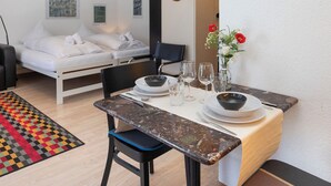 A hotel room with a bed, a dining table with chairs, a vase with flowers, and a mirror on the wall.