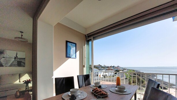 Een eethoek met een tafel voor twee personen, uitzicht op zee en een balkon met een hekwerk.