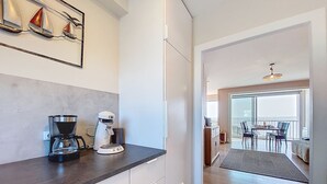 Een moderne keuken met een koffiezetapparaat en waterkoker, een eethoek met tafel en stoelen, en een balkon met uitzicht.