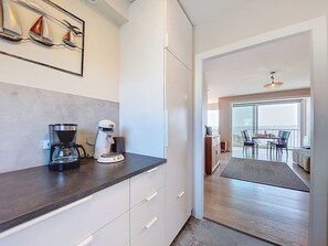 Eine moderne Küche mit Kaffeemaschine und Wasserkocher, ein Essbereich mit Tisch und Stühlen sowie ein Balkon mit Aussicht.