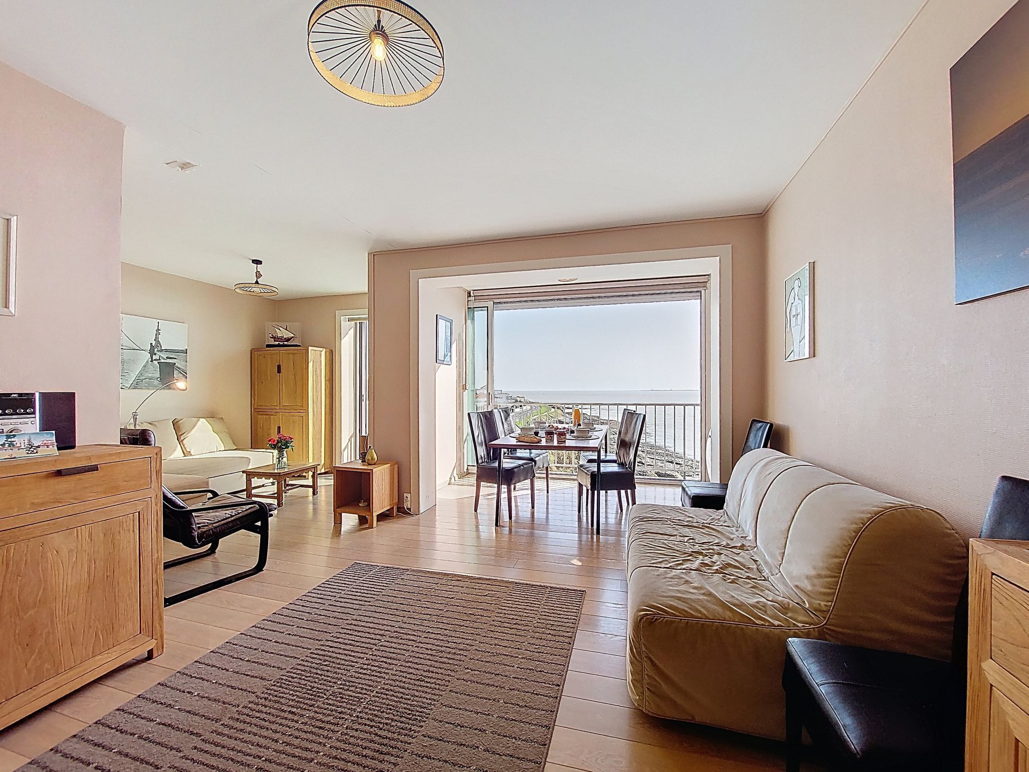 A spacious living area with a sofa, a dining table, and a view of the sea through a large window.