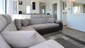 Un salon moderne avec un canapé gris, un petit tapis et un coin cuisine à l’arrière-plan.