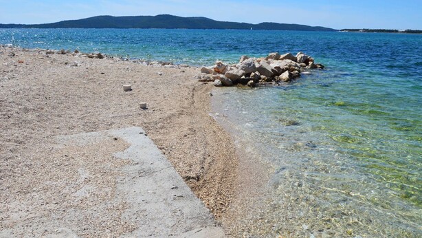 Une plage de galets avec une eau claire et une chaîne de montagnes qui se dessine à l'horizon.